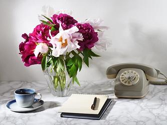 vase of peonies, cup of coffee, old-fashioned telephone and notebook on a table